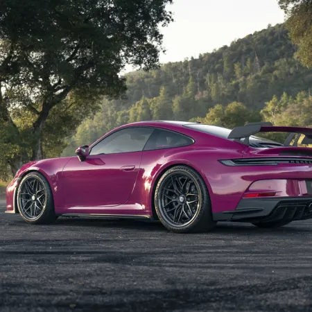 Sleek purple sports car parked on asphalt with trees and hills in the background during daytime.