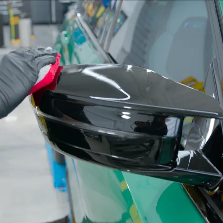 Person cleaning black car side mirror with a red cloth wearing a black glove in a garage.