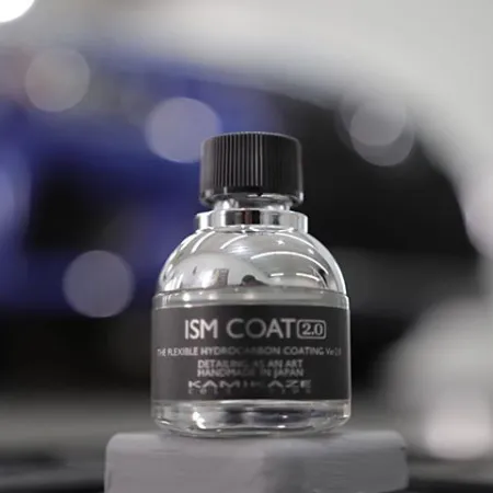 Close-up of ISM Coat 2.0 hydrocarbon coating bottle with blurred blue car background.