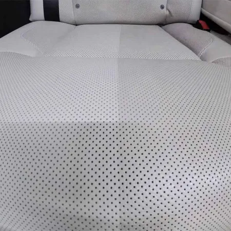 Close-up of a car seat showing a clean and dirty section of perforated light gray leather upholstery.
