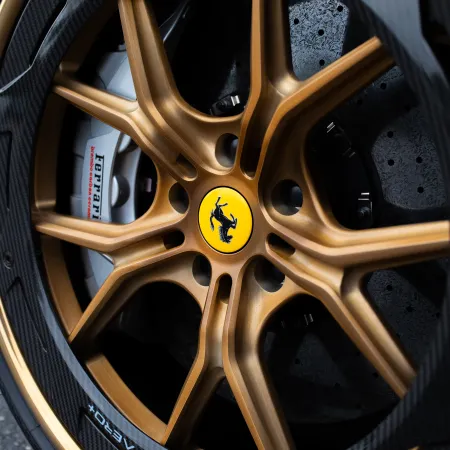 Close-up of a gold Ferrari alloy wheel with carbon fiber rim and yellow prancing horse emblem.
