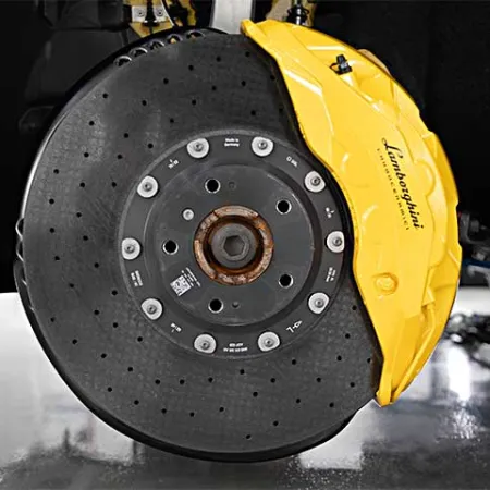 Close-up of a Lamborghini car's yellow brake caliper and carbon ceramic brake disc on a reflective floor.