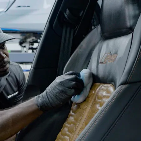 Person cleaning luxury car seat with gloves inside a vehicle featuring detailed leather upholstery.