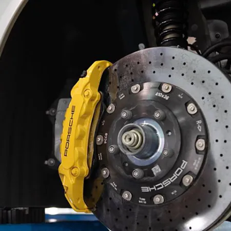 Close-up of a Porsche brake system featuring a yellow caliper and drilled carbon disc brake on a white car.