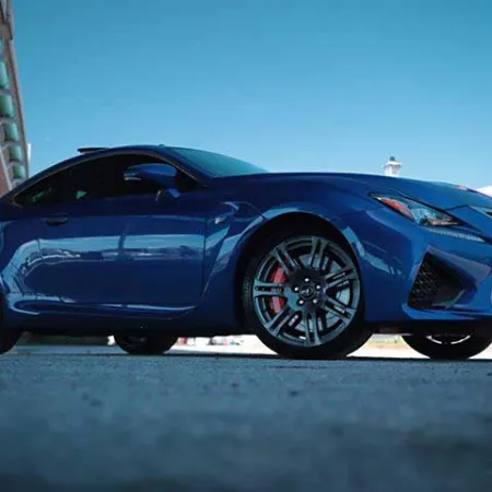 Low-angle view of a blue sports coupe parked outdoors near urban buildings under clear blue sky