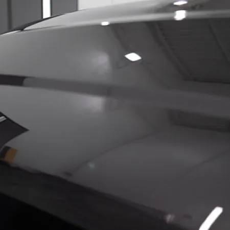 Close-up of a shiny black car hood reflecting ceiling lights in a garage setting.