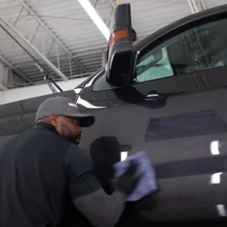 Man wearing cap polishing the side door of a black truck inside a well-lit garage.