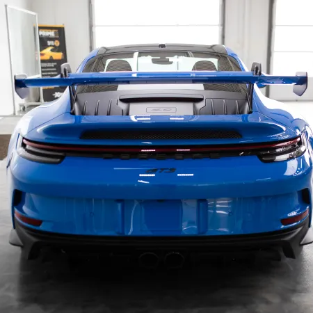 Rear view of a blue Porsche 911 GT3 with a large rear wing in a bright indoor showroom.