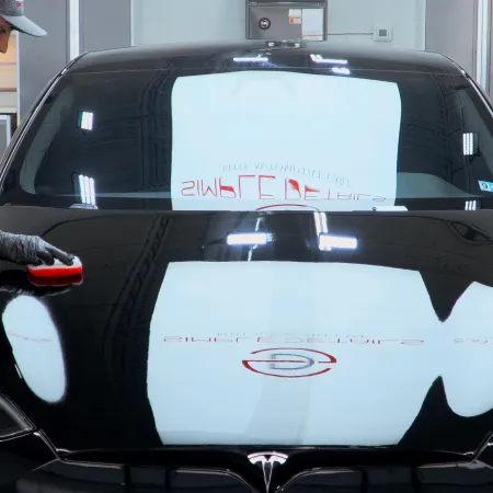 Technician polishing the hood of a shiny black Tesla car in a modern automotive workshop.