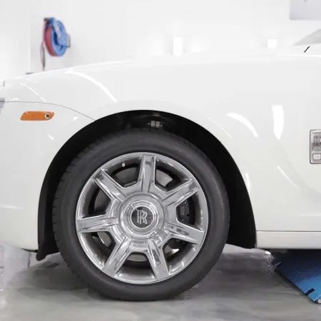 Close-up of a white Rolls-Royce car wheel with shiny chrome rim in a clean garage with repair equipment.