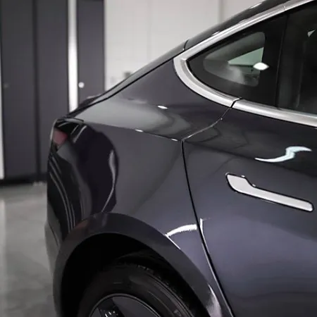 Close-up of a sleek black car's rear side panel and wheel in a modern garage setting.