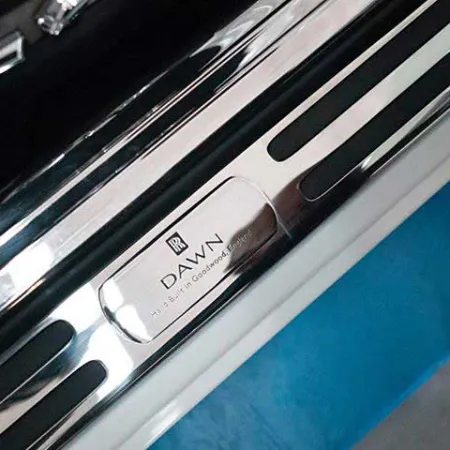Close-up of Rolls-Royce Dawn stainless steel door sill plate with engraved branding and model name.