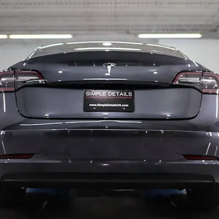 Rear view of a dark Tesla Model 3 parked indoors with Simple Details license plate in a garage setting
