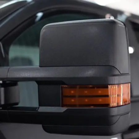 Close-up of a black truck's side mirror with integrated amber turn signal light and reflective surface.