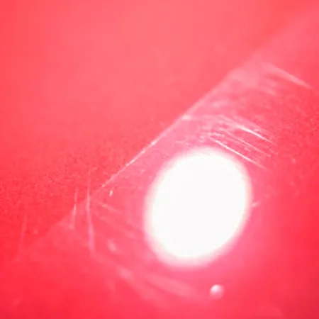Close-up of a red surface with a bright white reflective spot highlighting fine scratches and texture.