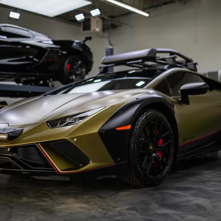 Gold and black Lamborghini sports car with roof rack inside a garage with another black car in background.
