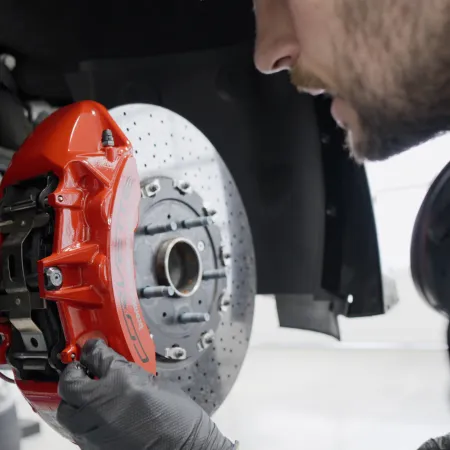 Mechanic inspecting a red brake caliper and drilled brake disc on a car wheel in a garage.