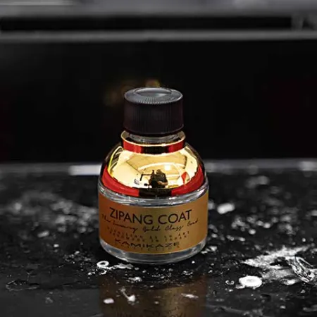 Small glass bottle labeled ZIPANG COAT on black surface with red container edges and water droplets.