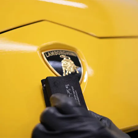 Close-up of a yellow Lamborghini hood with a detailer polishing the emblem with a cloth.