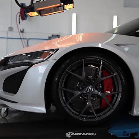 Close-up of a white sports car front wheel with black alloy rim and red brake caliper in a garage.