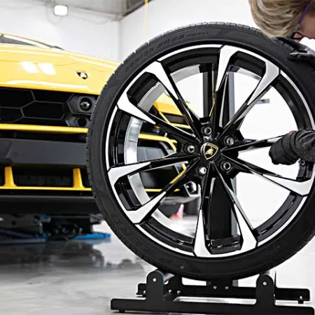 Mechanic adjusting a sleek black and silver Lamborghini wheel next to a yellow Lamborghini Urus in a garage.