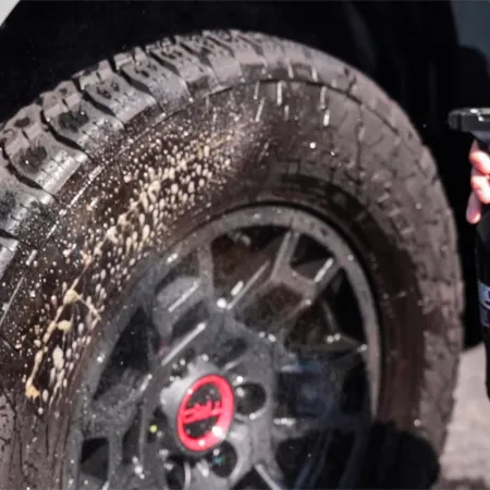 Person spraying tire cleaner on a muddy car tire with black alloy wheel and red hub detail.