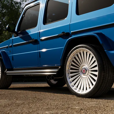 Blue luxury SUV with shiny multi-spoke silver rims parked on asphalt near trees in daylight.