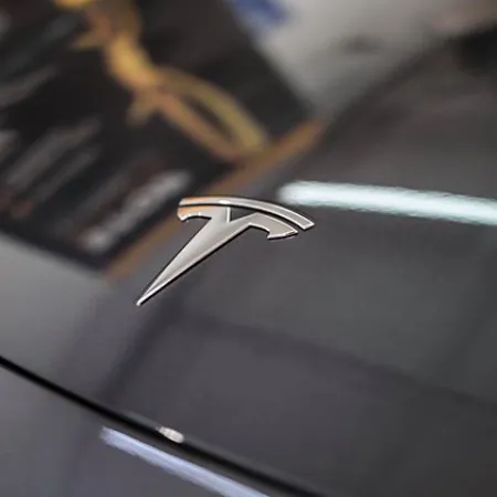 Close-up of a Tesla logo on a sleek black electric car hood with glossy reflection.