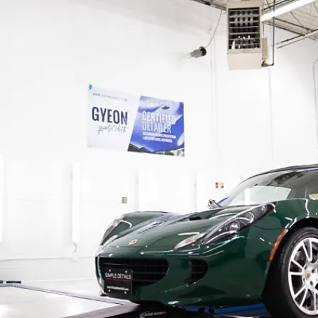 Green sports car inside a bright automotive workshop with white walls and certification posters.