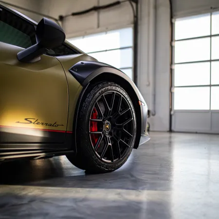 Close-up of a matte gold Lamborghini Sterrato front wheel and side mirror in a bright garage.