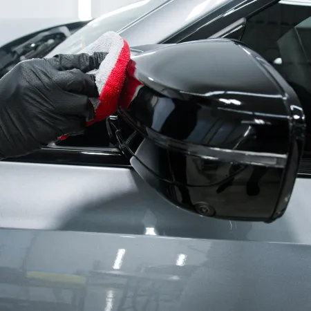 Hand in black glove polishing a black car side mirror with red and white cloth on a silver vehicle.