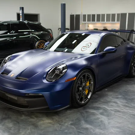 Matte blue Porsche sports car with black rims and yellow brake calipers in a polished garage setting.