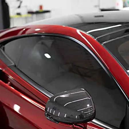 Close-up of a sleek red sports car with tinted windows and carbon fiber side mirror in a garage.
