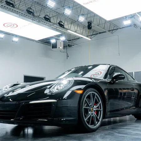 Black Porsche sports car in a bright, modern showroom with polished concrete floor and industrial lighting.