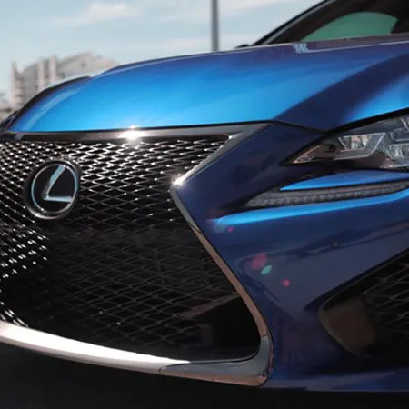 Close-up of a blue Lexus car front grille with emblem and sleek headlight design in daylight.
