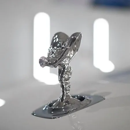 Close-up of a shiny silver Rolls-Royce Spirit of Ecstasy hood ornament on a white car.