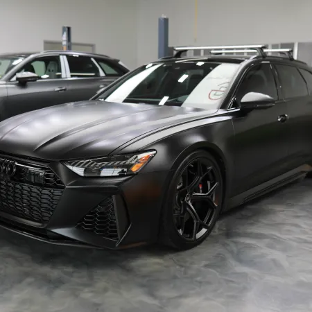 Sleek matte black Audi sports car parked in a modern garage with polished concrete floor and lifted vehicles.
