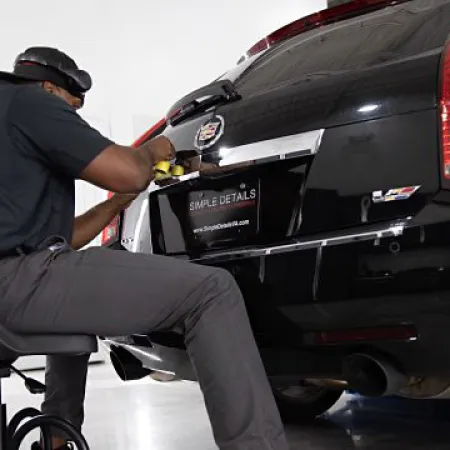 Man detailing the rear of a black Cadillac car in a clean indoor garage using a yellow cloth.