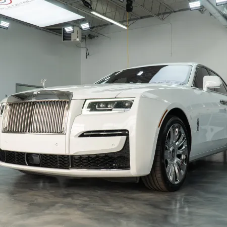 White Rolls-Royce luxury car parked indoors with chrome accents and distinctive grille under bright lighting.
