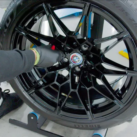 Technician wearing gloves working on a glossy black alloy car wheel with Pirelli tire in a workshop.
