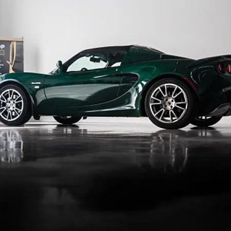 Dark green sports car parked indoors with glossy floor reflection and white wall background.