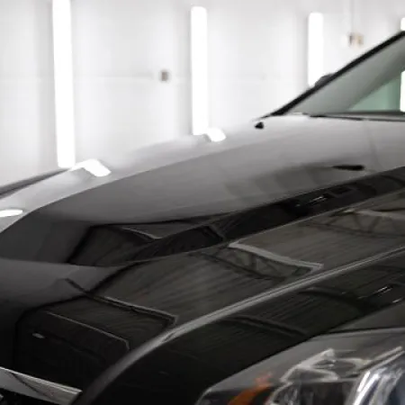 Close-up of a shiny black luxury car hood and front headlight in a well-lit garage.
