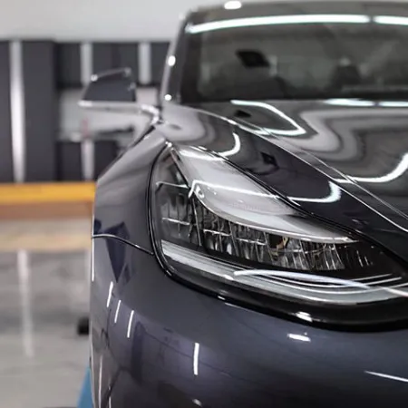 Close-up of a sleek black car headlight reflecting showroom lights on a polished surface.