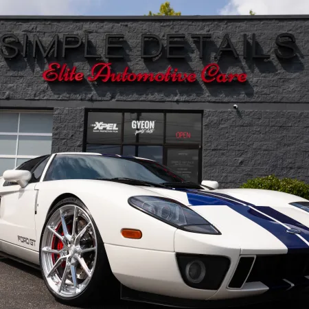 White Ford GT with blue racing stripes parked outside Simple Details Elite Automotive Care shop.