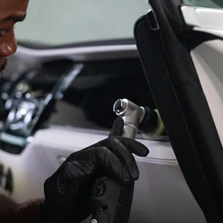 Man wearing black gloves using a power tool to work on the interior of a luxury car door.