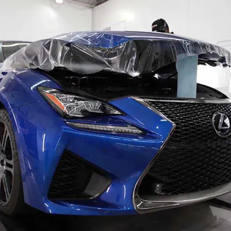 Blue Lexus sports car with damaged front end covered in protective plastic inside a garage.