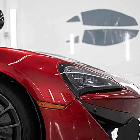 Close-up of a shiny red sports car front with detailed headlight and wheel in a bright garage.