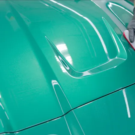Person wearing gloves cleaning and polishing a shiny teal car hood with a white and red cloth.