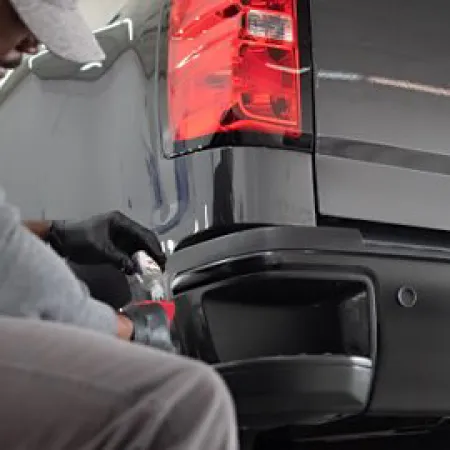 Technician wearing gloves installing or repairing a tail light on a black pickup truck in a garage