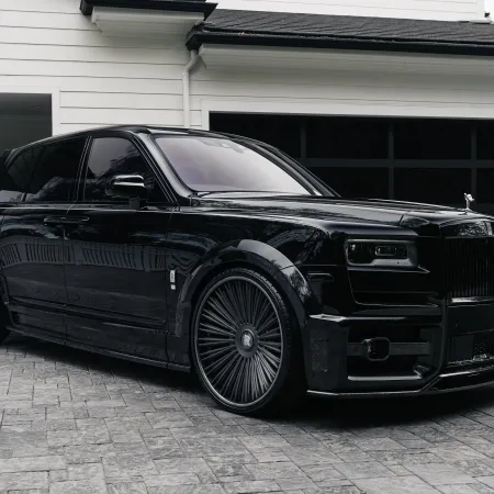 Glossy black luxury SUV parked on stone driveway in front of modern white house with black garage doors.